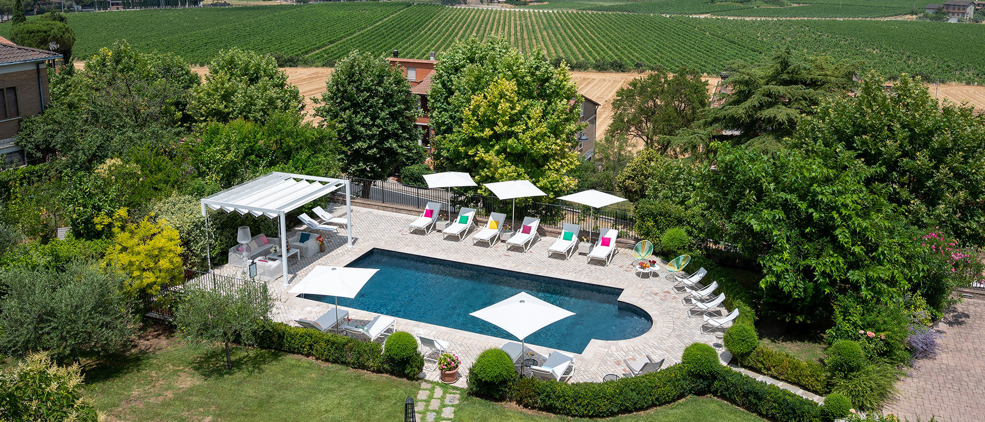 Piscina elegante in boutique hotel umbro immerso nel verde, con lettini bianchi, ombrelloni e vista su vigneti